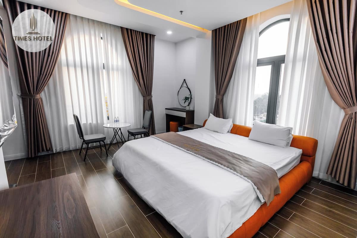 A hotel room with a large bed, a desk, a chair, and a view of the city.