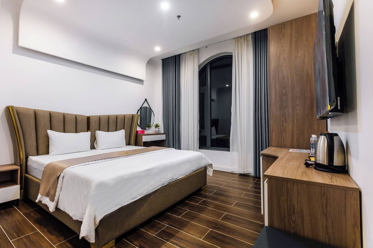 A modern hotel room with a large bed, a wooden desk, a flat-screen TV, and a window with curtains.
