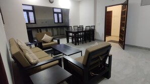 Un espace de vie comprenant des canapés, une table basse et une table à manger avec des chaises. Il y a également une cuisine avec une fenêtre et une porte donnant sur une autre pièce.