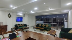 Un vaste espace de vie comprenant une grande table basse en bois, deux canapés verts, un meuble en bois et un téléviseur à écran plat fixé au mur.