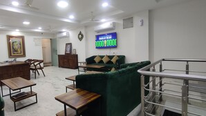 Un hall d’hôtel avec un comptoir d’accueil, des canapés verts, des tables en bois et un escalier.