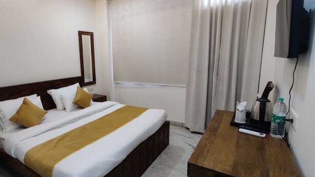 A hotel room with a bed, a wooden nightstand, a bedside table with a bottle and a remote control, and a wall-mounted TV.