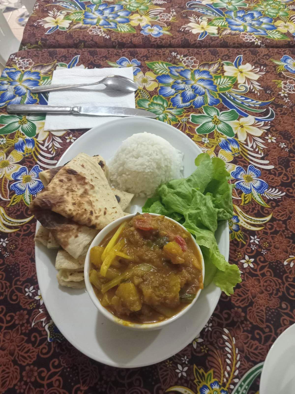 Un plato con arroz, pan plano, una preparación de verduras y lechuga sobre un mantel estampado.