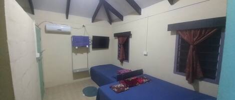 Une petite chambre simple, avec deux lits, une fenêtre avec des rideaux, un climatiseur et un téléviseur.