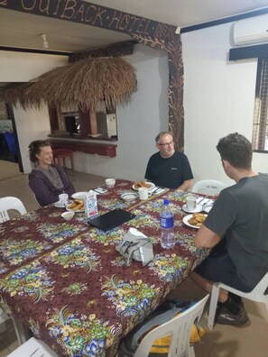 Un comedor con una mesa dispuesta para cuatro personas, una estructura de techo de paja y un letrero que dice 'OUTBACK HOTEL'.