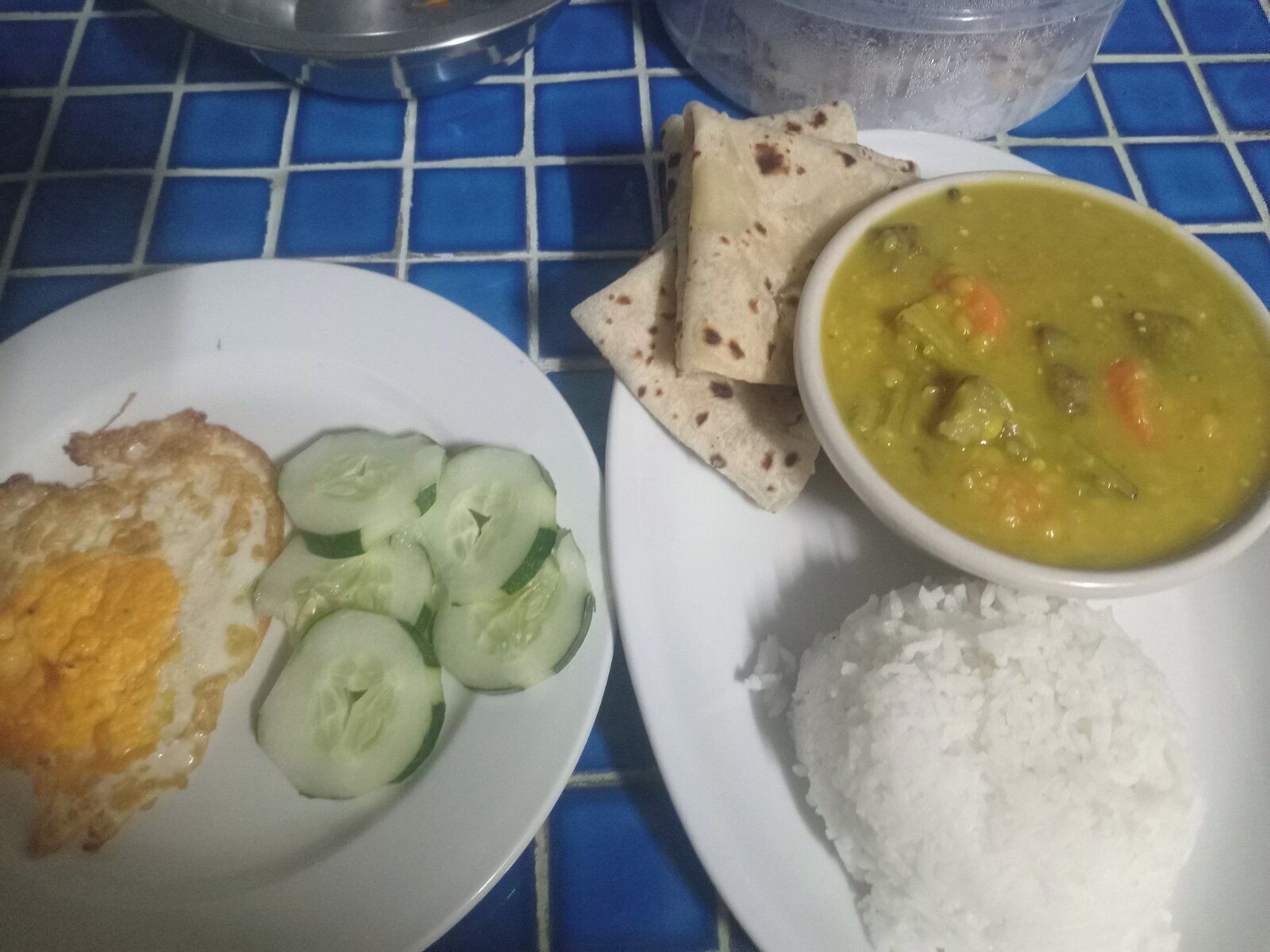 A plate with a fried egg, cucumber slices, a bowl of soup, flatbread, and white rice.