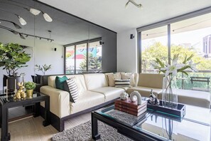 Un salon moderne avec un canapé en cuir, une table basse en verre et une grande fenêtre donnant sur la ville.