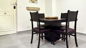 A dining area with a dark wooden table and four chairs, a woven basket on the table, a white door, and a wall-mounted decorative piece.