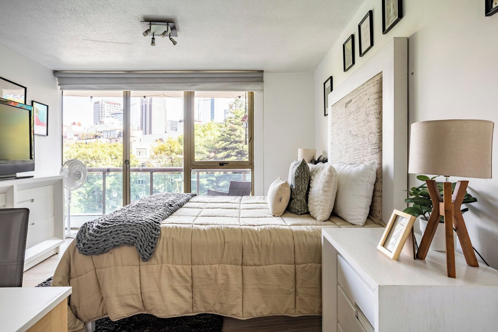 A bedroom with a bed, bedside table, lamp, and a window with a city view.