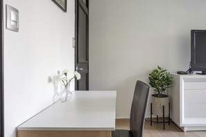 A minimalist room with a white table, a chair, a potted plant, and a television on a stand. - Cozy 2-bedroom apartment in vibrant Ciudad de México with WiFi (Ciudad de México)