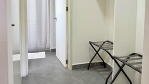 A hallway with a white door leading to a bathroom with a shower curtain. There is a metal drying rack against the wall.