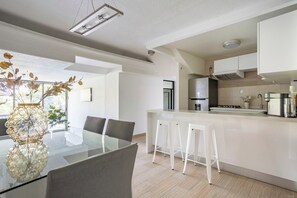 A modern kitchen with a central island, white bar stools, and a dining table with chairs.