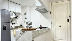 A modern kitchen with white cabinetry, a marble countertop, a built-in microwave, and a stainless steel refrigerator.