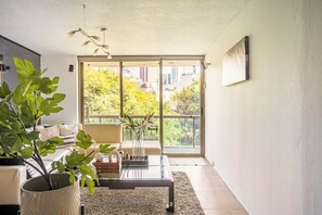 A modern living room with a glass coffee table, a sofa, and a large window with a view of trees and buildings. - Cozy 2-bedroom apartment in vibrant Ciudad de México with WiFi (Ciudad de México)