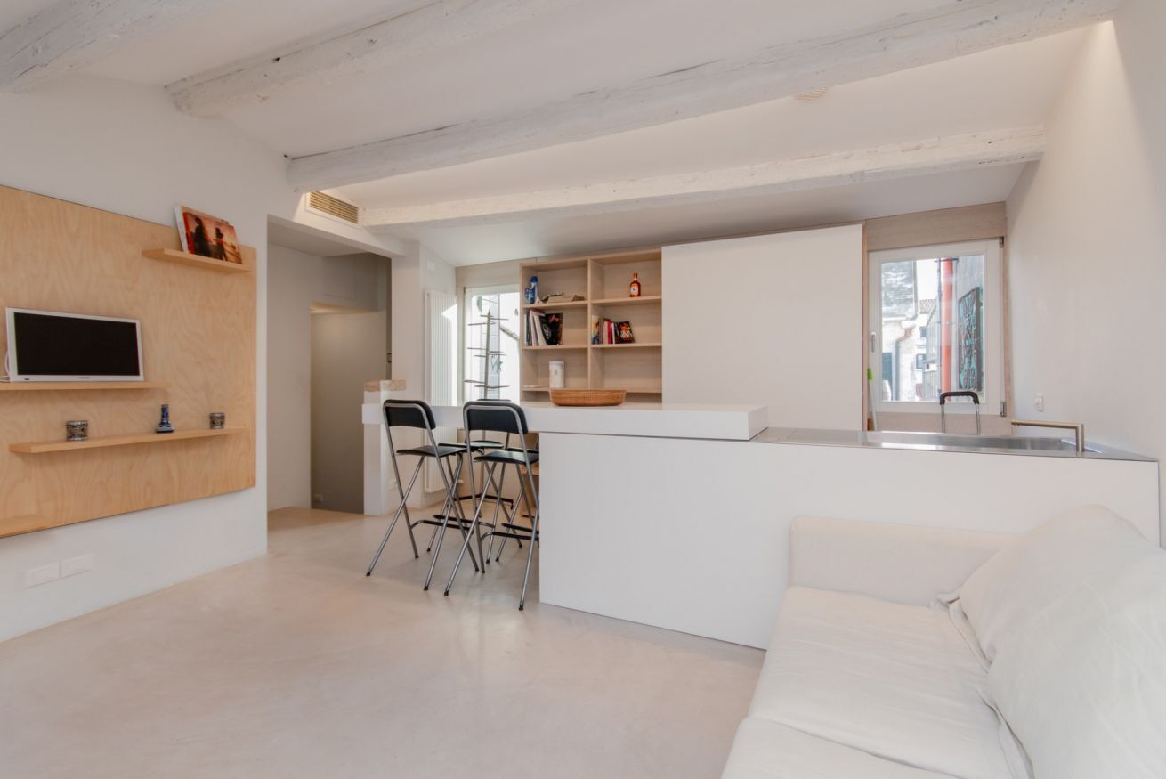 A modern kitchen with a white countertop, two black chairs, and a white sofa.
