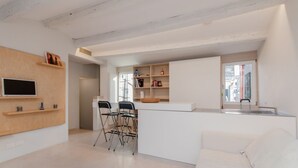 Eine moderne Küche mit einer weißen Arbeitsplatte, zwei schwarzen Stühlen und einem weißen Sofa.