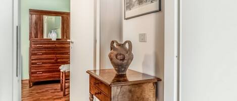 A hallway with a wooden dresser, a small table with a vase, and a framed picture on the wall.