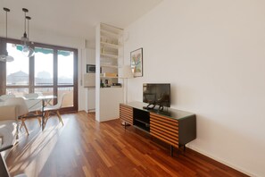 En moderne stue med spiseplads, et fjernsyn og et køkkenområde med hylder.