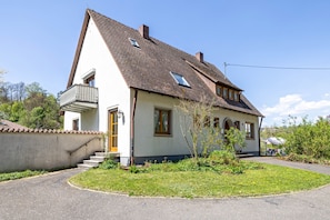 A two-story house with a sloped roof, a balcony, and a small garden area.