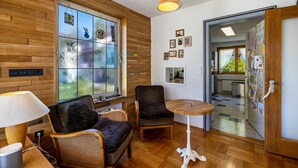 Ein Zimmer mit Holzwand, einem großen Fenster, einem Tisch, zwei Stühlen, einer Lampe und einem Kühlschrank.