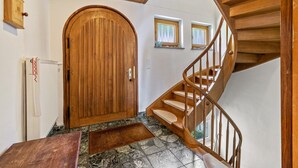 Eine Holztreppe führt zu einer zweiten Etage, eine große Holztür und ein Heizkörper an der Wand.