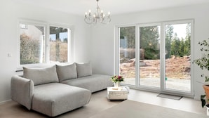 Un salon moderne avec un canapé d’angle gris, un lustre et de grandes portes-fenêtres coulissantes.