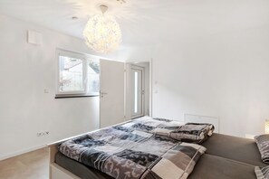 Une chambre à coucher avec un lit, une fenêtre, une porte et un luminaire suspendu.