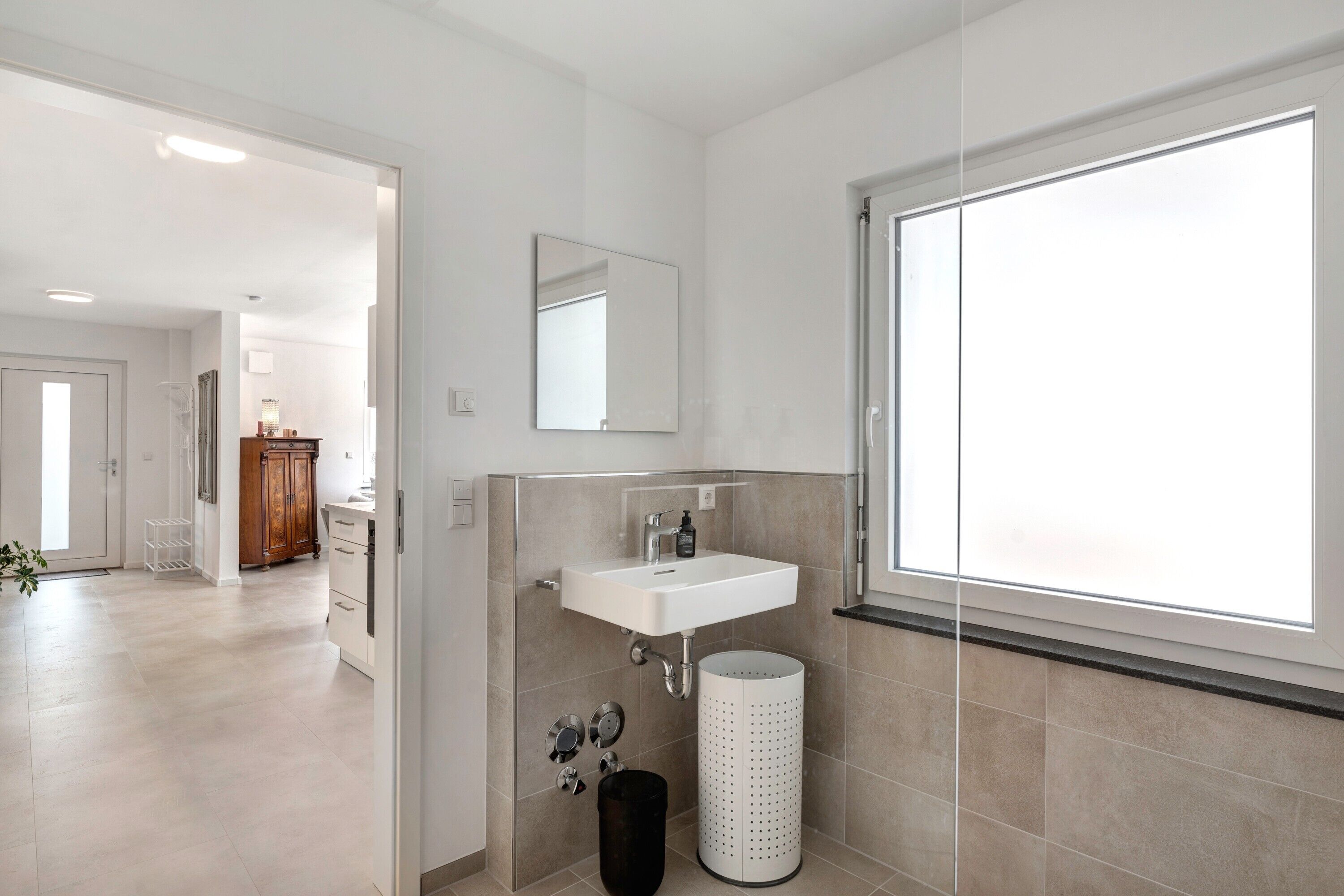 A modern bathroom with a sink, mirror, and window.