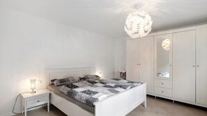 Une chambre à coucher comprenant un lit, une table de chevet, une lampe, une armoire et un luminaire décoratif au plafond.