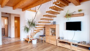 Een moderne woonkamer met een houten trap, een flatscreen televisie en een plant.