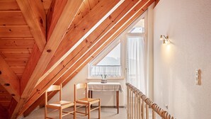 An attic room with wooden beams, a window with curtains, a table with chairs, and a railing. - Apartment 'Schillingblick' with Shared Garden, Balcony and Wi-Fi (Titisee-Neustadt)
