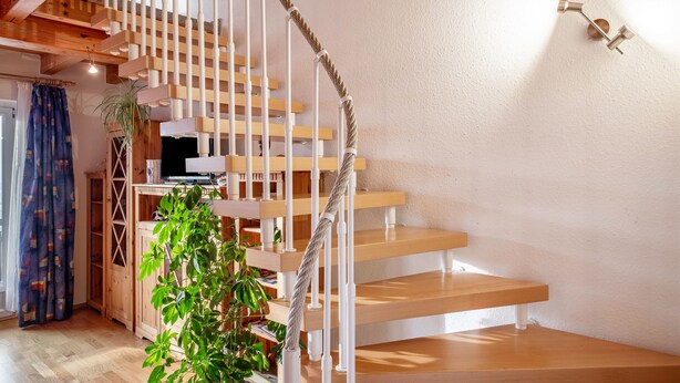 A spiral staircase with wooden steps and white balusters, a plant in a wooden crate, and a wall-mounted light fixture. - Apartment 'Schillingblick' with Shared Garden, Balcony and Wi-Fi (Titisee-Neustadt)