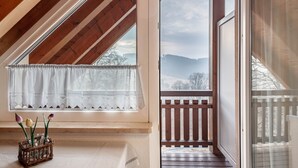 A room with a sloped ceiling, a window with a white curtain, a wooden balcony, and a wicker basket with flowers. - Apartment 'Schillingblick' with Shared Garden, Balcony and Wi-Fi (Titisee-Neustadt)
