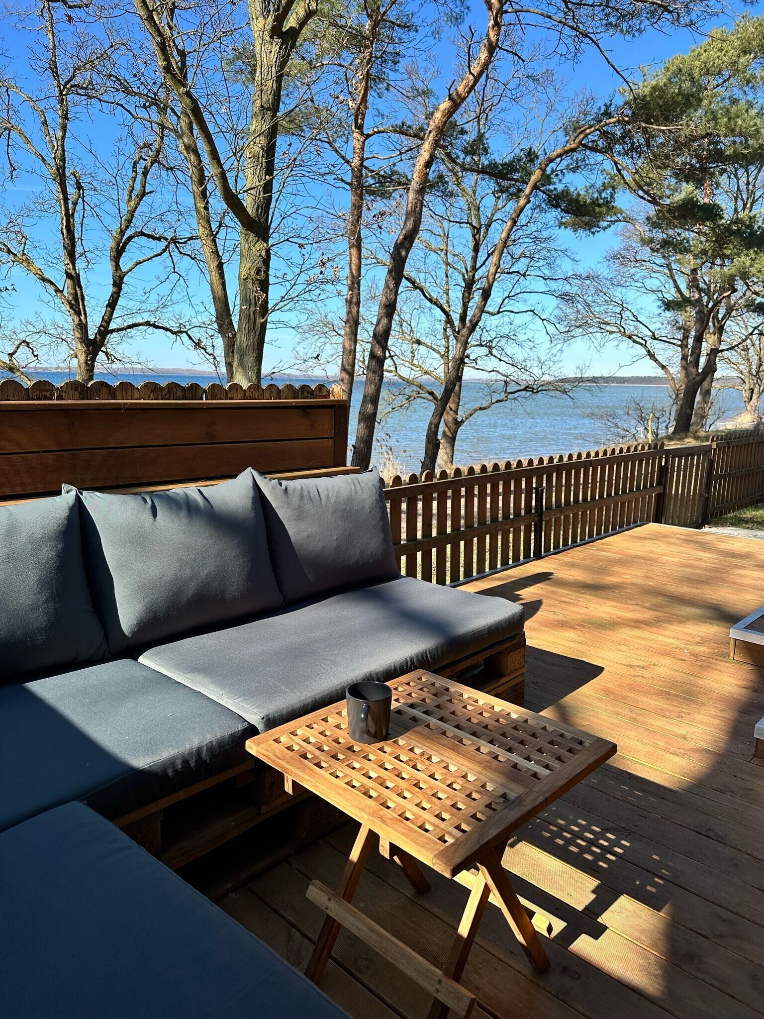 Una terraza de madera con un sofá y una mesa, con vista a un cuerpo de agua.