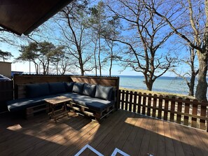 A wooden deck with a built-in sofa and table, overlooking a body of water and trees. - Surf Bungalow in Prime Location with Sea View, Private Terrace, and Wi-Fi (Am salzhaff)