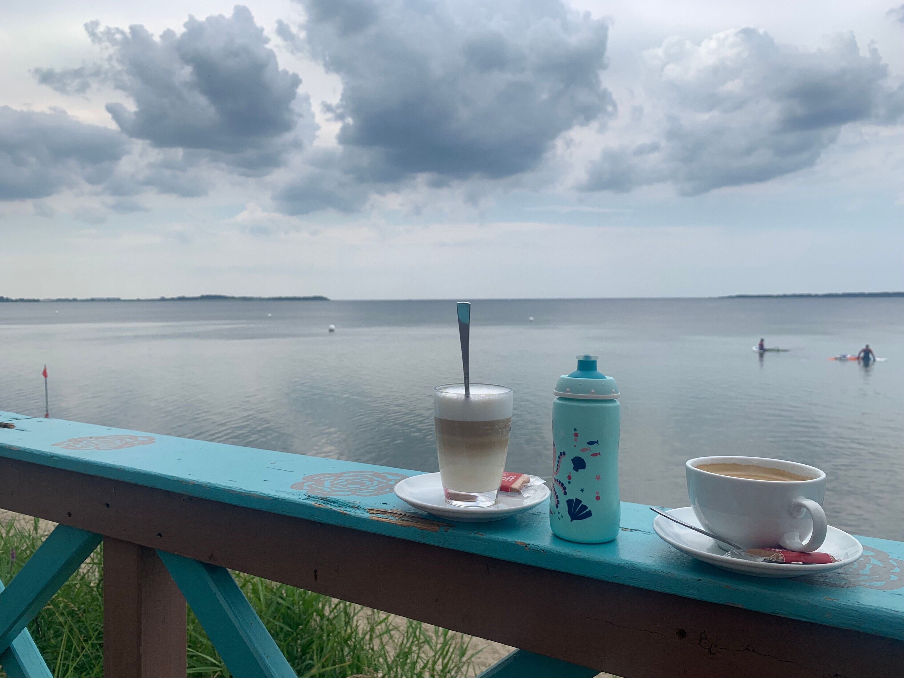 Vista de un lago con un muelle de madera, un vaso de café helado y una botella de agua.