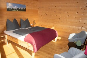 Un dormitorio de cabaña de madera con una cama, almohadas, una silla y una mesita.