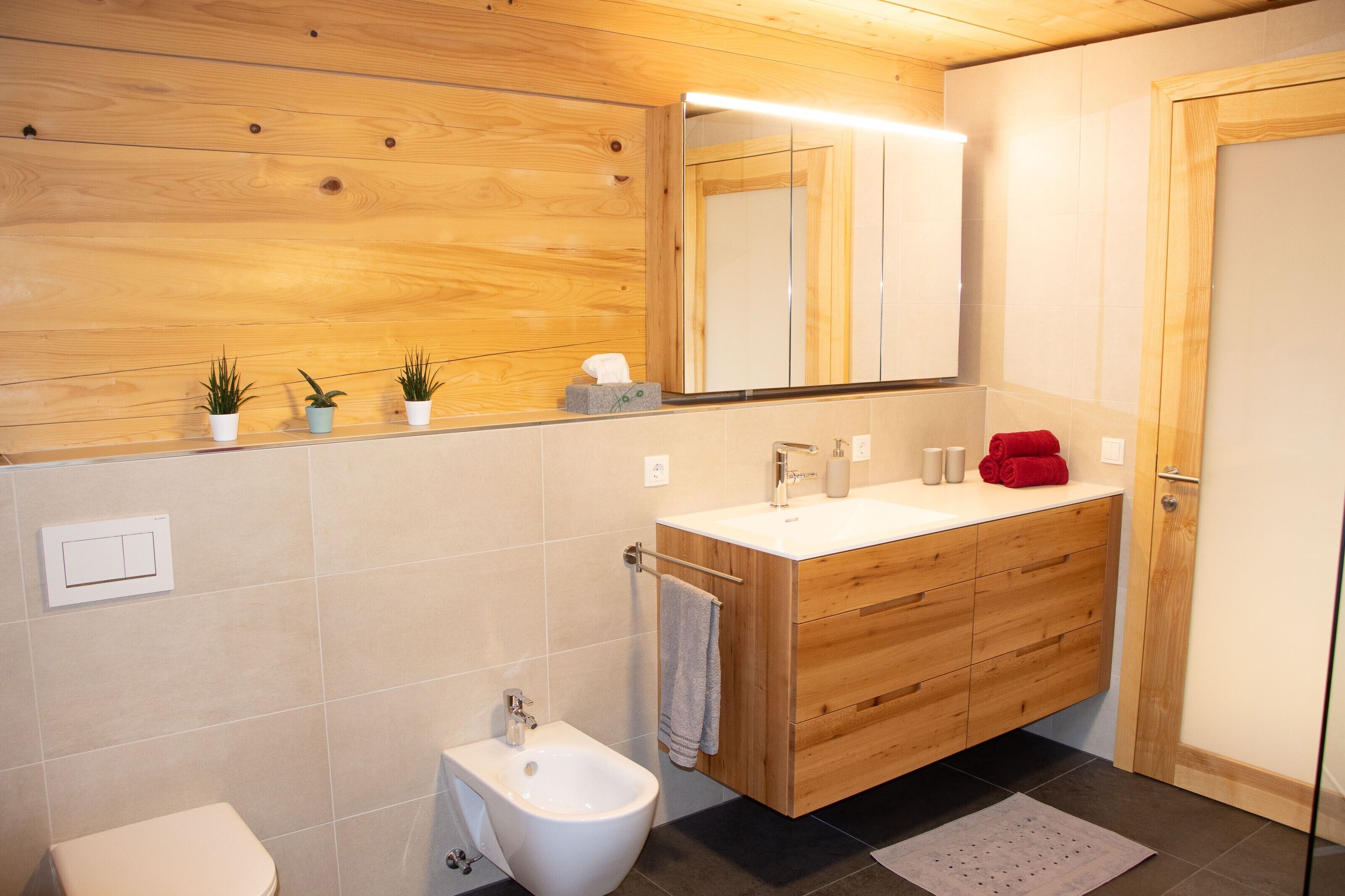 Een moderne badkamer met een houten wastafelmeubel, een toiletbril, een toilet en een spiegel boven het meubel.