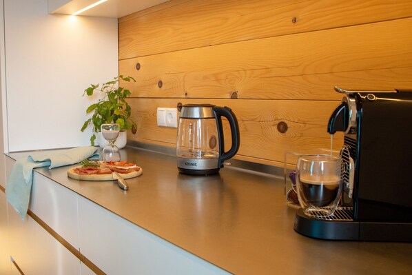 A modern kitchen with a coffee maker, a glass of coffee, and a pizza on the counter.