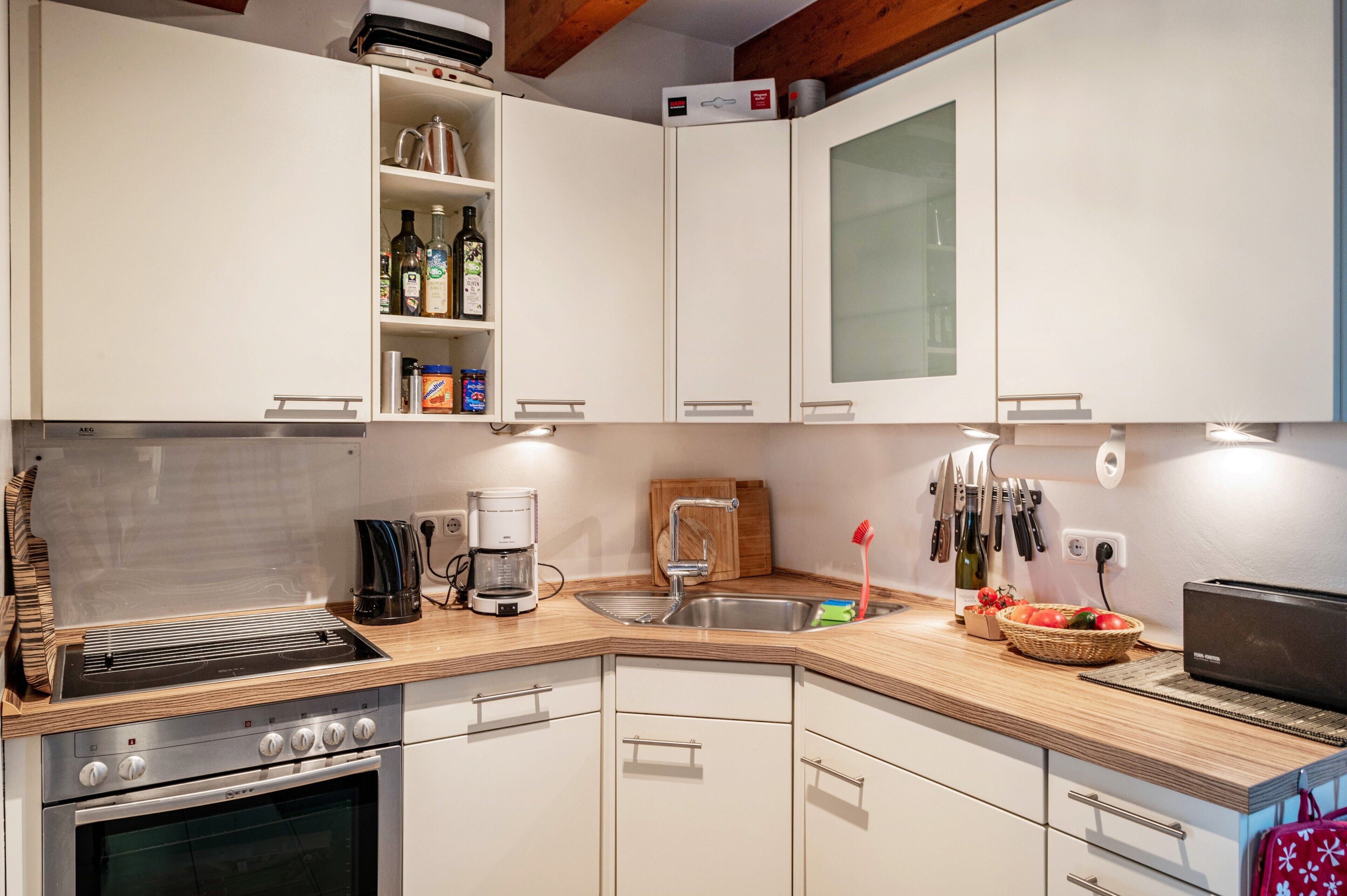 Una cocina moderna con armarios blancos, horno empotrado, cafetera y lavabo.