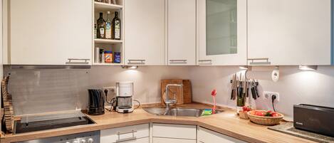 Una cocina moderna con armarios blancos, horno empotrado, cafetera y lavabo.