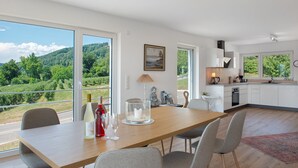 A modern kitchen with a dining area, large windows, and a view of a vineyard. - Aura Upper Floor Holiday Home with Lake View, Alpine Panorama, Balconies, Garden & Wi-Fi (Bodman-Ludwigshafen)