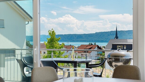 A balcony with a table, chairs, a grill, and a view of the lake and buildings. - Aura Upper Floor Holiday Home with Lake View, Alpine Panorama, Balconies, Garden & Wi-Fi (Bodman-Ludwigshafen)
