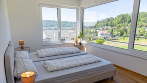 A bedroom with a large window, a bed, a bedside table with a lamp, and a view of a green landscape. - Aura Upper Floor Holiday Home with Lake View, Alpine Panorama, Balconies, Garden & Wi-Fi (Bodman-Ludwigshafen)