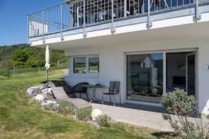 A modern house with a balcony, a patio with outdoor furniture, and a large sliding glass door leading to a covered area.