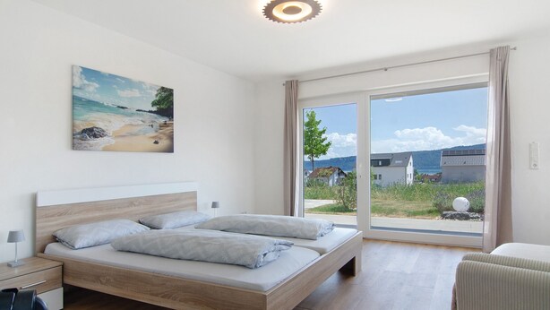 Een slaapkamer met een bed, een bureau en een stoel. Er hangt een schilderij aan de muur en er is uitzicht op het buiten.