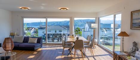 A spacious living area with a large window, a dining table, and a sofa.