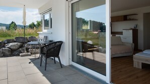 Een moderne kamer met een schuifglazen deur naar een patio met een tafel, stoelen, een bank en een zichtbare keuken.