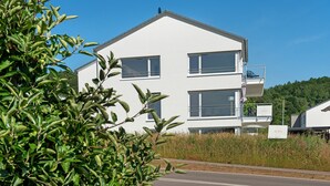 Een gebouw met twee verdiepingen, balkons, een heldere lucht en groenvoorstelling op de voorgrond.