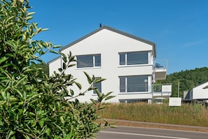 Ein zweistöckiges Gebäude mit Balkonen, blauem Himmel und Grünpflanzen im Vordergrund.